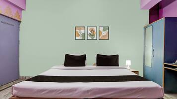 Quarto de hotel com cama, duas almofadas, mesa de cabeceira com abajur e três quadros na parede.