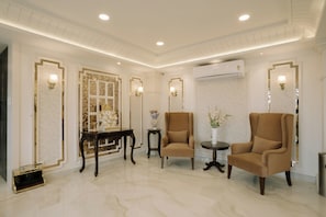 A spacious room with a marble floor, two brown armchairs, a small round table, and a decorative mirror with gold accents. - Hotel Maneybung (Gangtok)