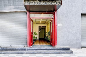 Entrada d'un edifici amb una porta vermella, un paviment de pissos i plantes en testos a l'interior.