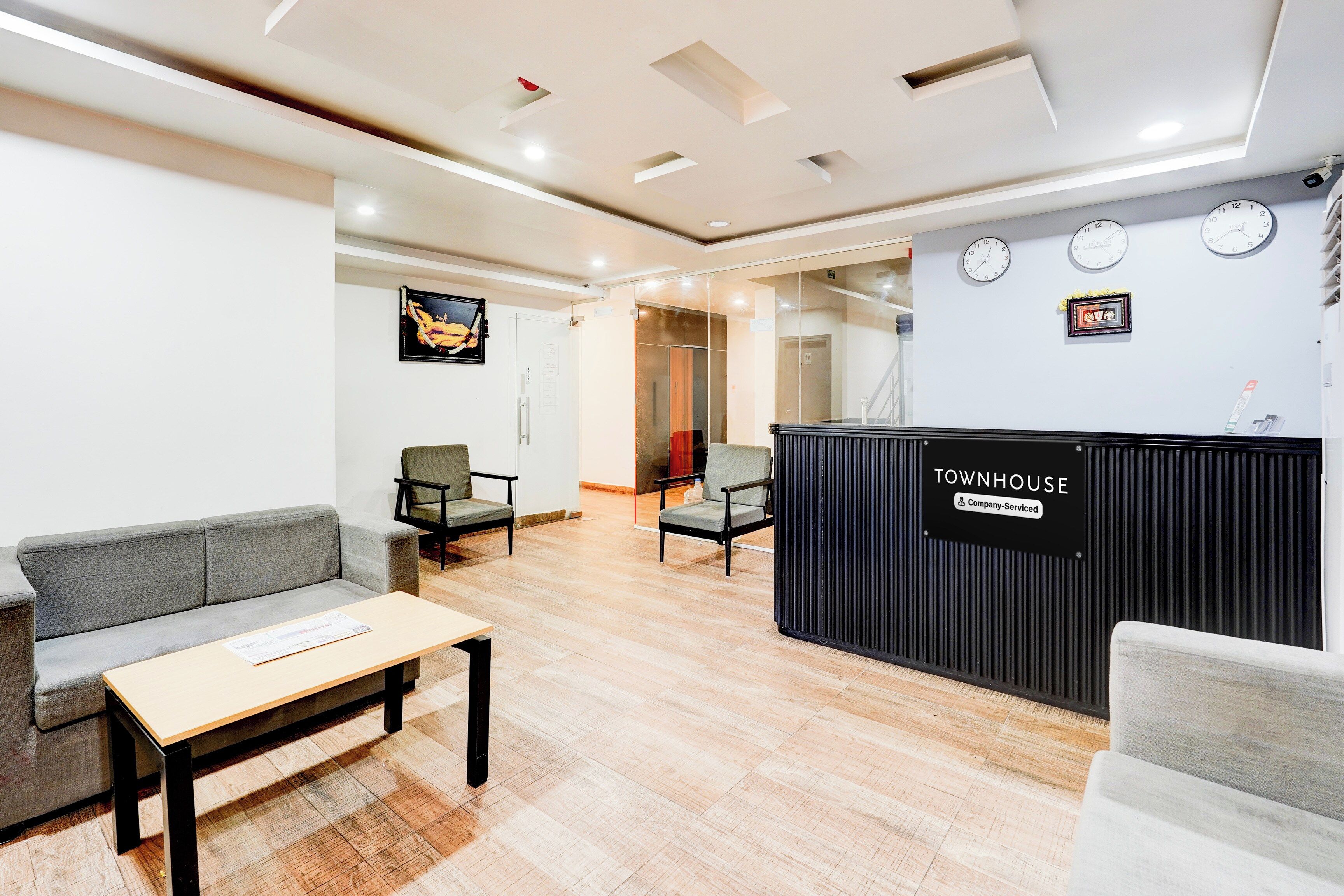 A reception area with a reception desk labeled 'TOWNHOUSE' and 'Company Serviced.' There are two sofas and a table with a newspaper.