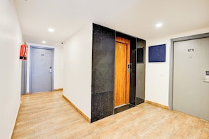 Un pasillo con piso de madera, una puerta azul y un extintor de incendios en la pared.