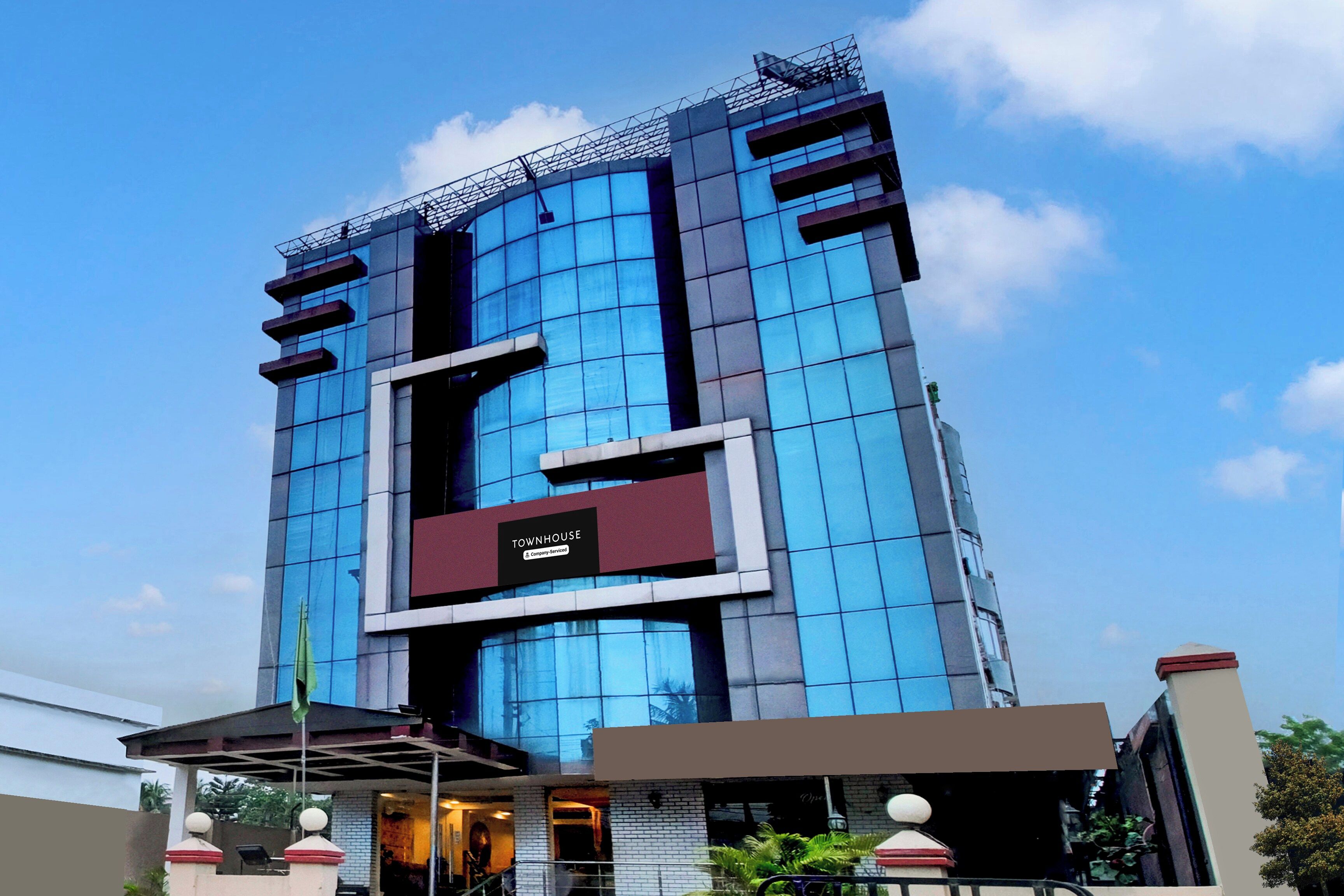 A modern high-rise building with a prominent glass facade, a central entrance, and a sign indicating it is a company-serviced property.