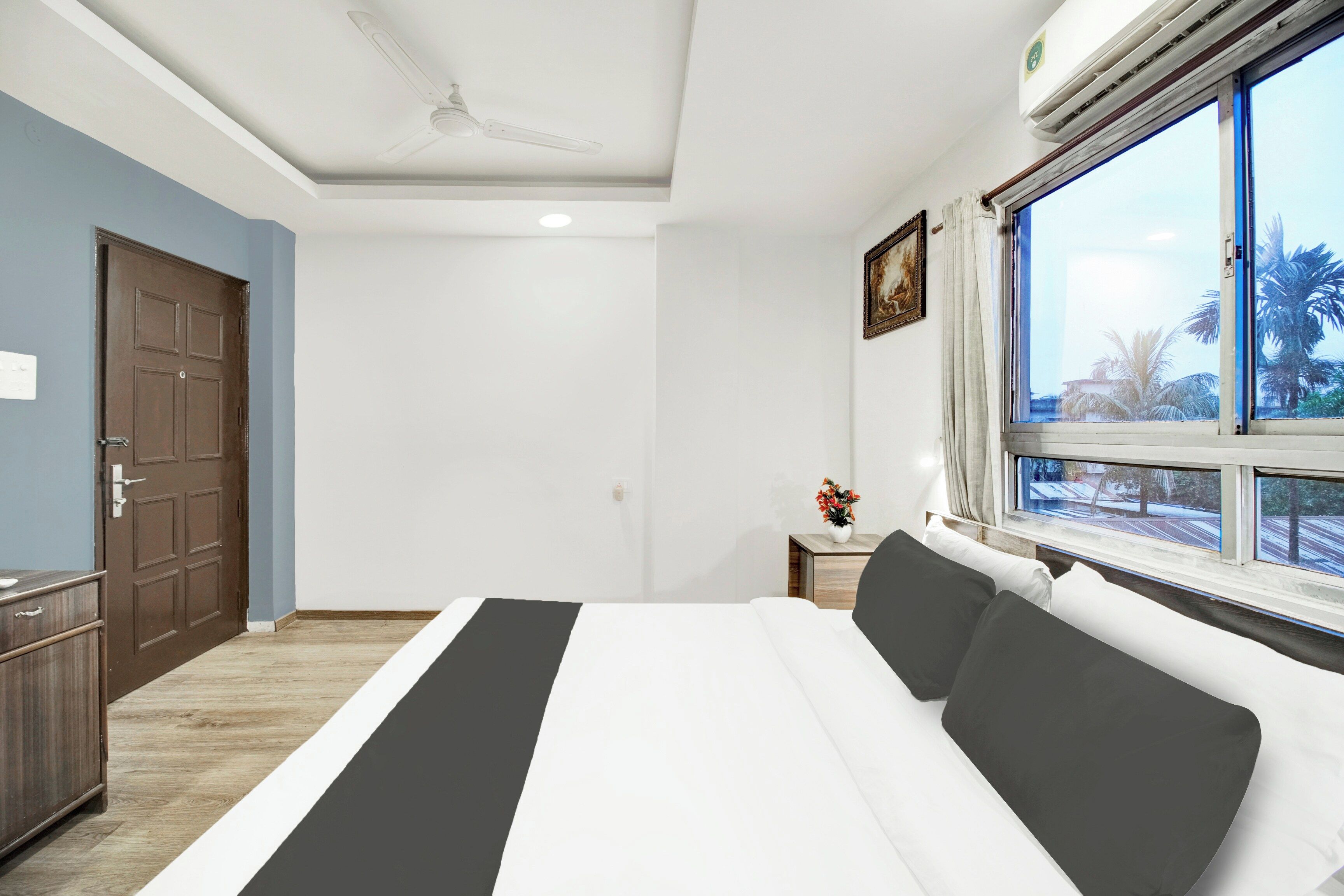 Een hotelkamer met een bed, een raam met uitzicht, een plafondventilator en een deur.