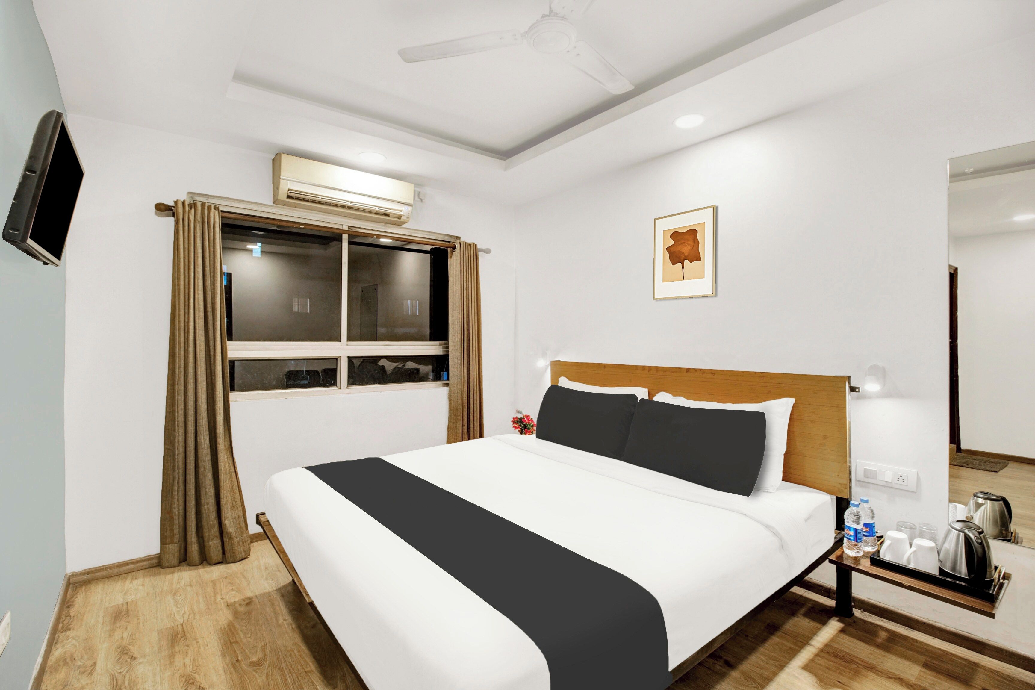 Una camera d'albergo con un letto, un comodino con un bollitore, un quadro incorniciato appeso al muro e una finestra con tende.