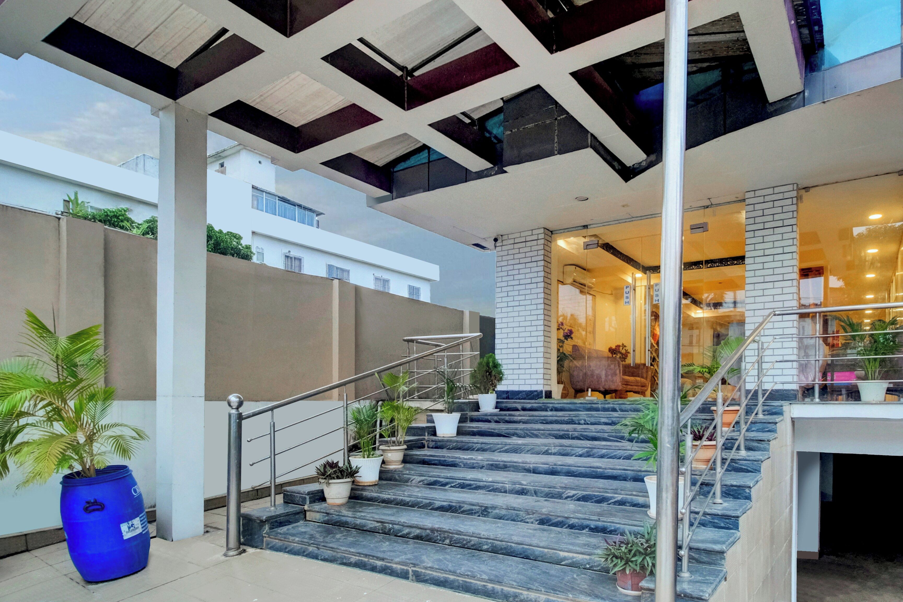 A modern building with a staircase leading to an upper level, a blue barrel, and potted plants.