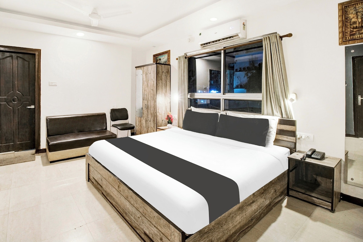 Habitación de hotel con una cama grande, una mesita de noche con teléfono, una ventana con cortinas, un armario y un banco.