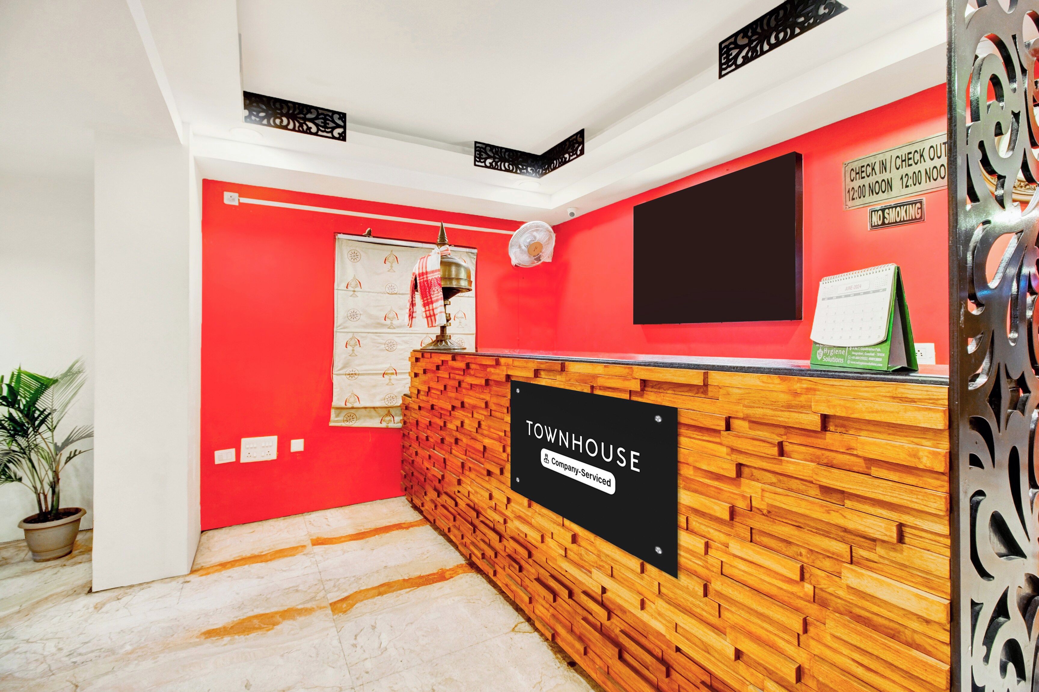 A reception area with a red wall, a wooden reception desk, a black sign reading 'TOWNHOUSE Company-Serviced', and a calendar on the wall.