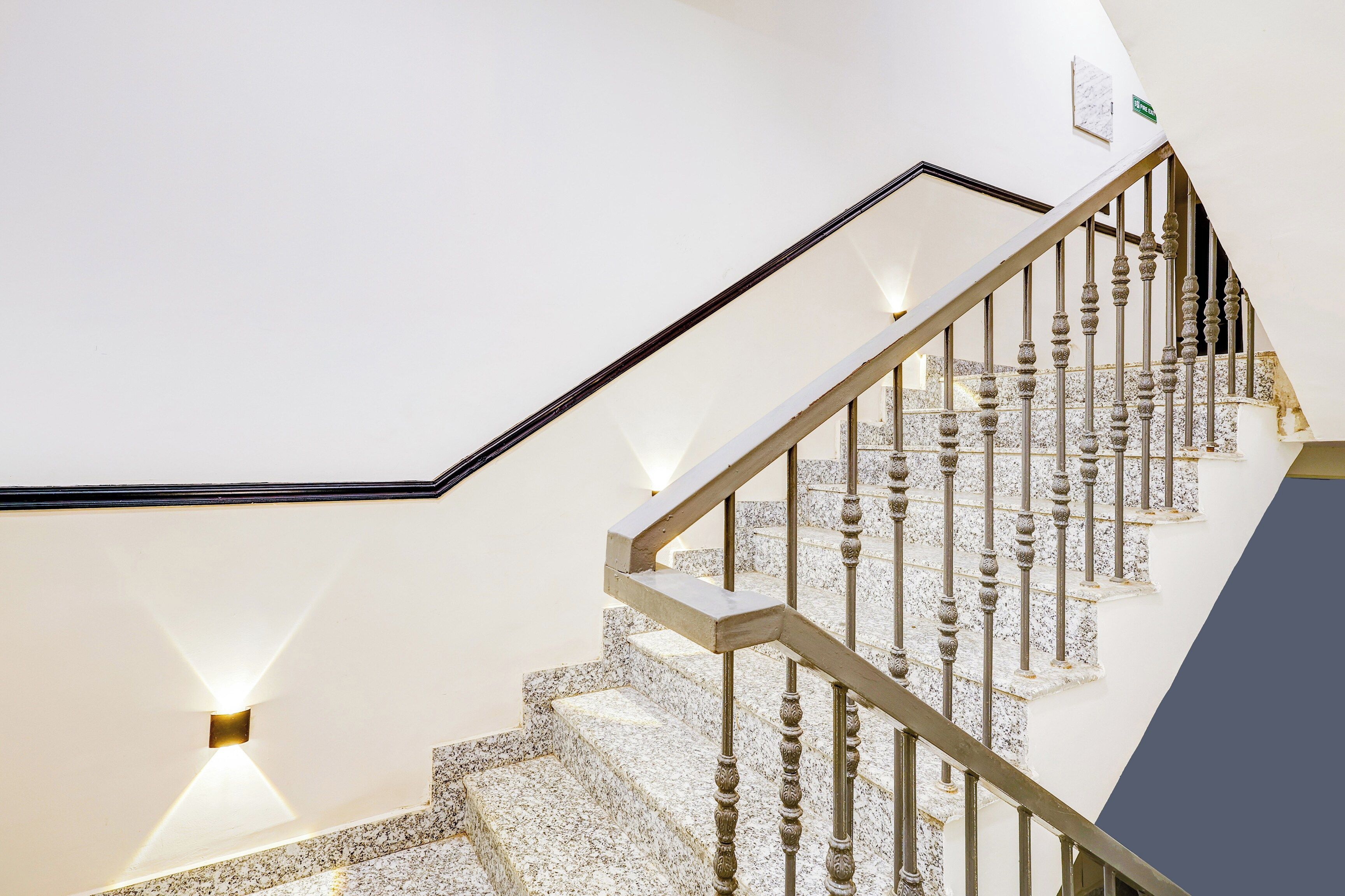 A staircase with a white wall and a marble floor, leading to a landing with a light fixture.