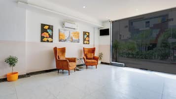 Eine Lobby mit zwei Ledersesseln, einer Zimmerpflanze und Wandkunst.