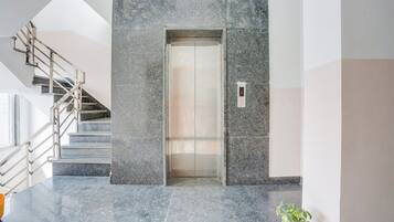 A modern elevator with a digital display, a marble-tiled wall, and a staircase with metal railings.