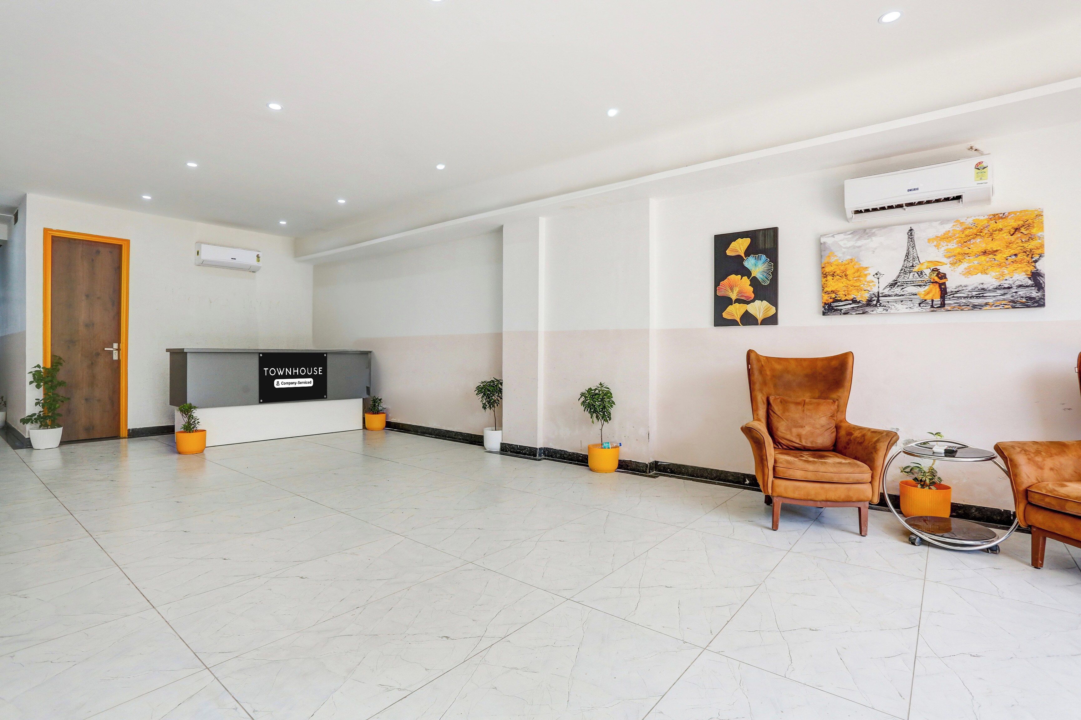 Un vestíbulo amplio con una mesa de recepción, un sillón de cuero marrón y plantas en macetas.