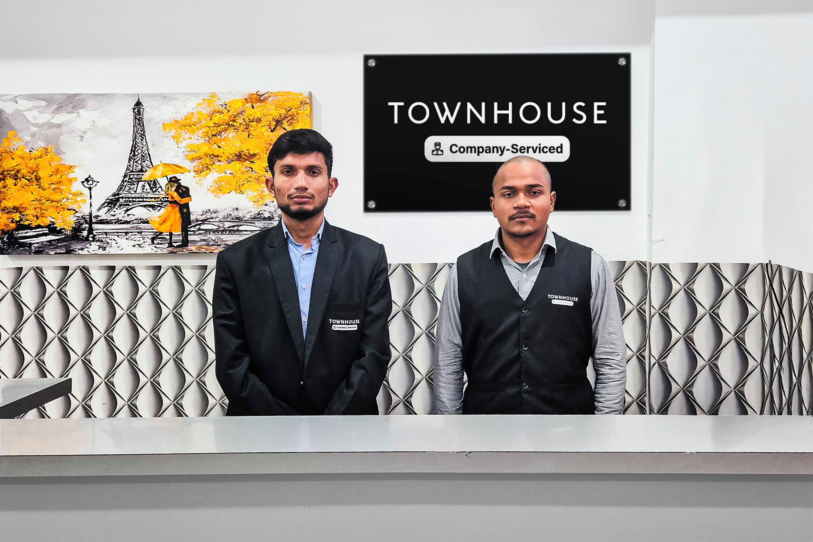 Dos personas frente a una recepción con un cartel que dice 'Townhouse' y una etiqueta que indica 'Servicio de empresa'.