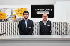 Two individuals standing in front of a reception desk with a 'Townhouse' sign and a 'Company-Serviced' label. - Townhouse Sector 69 Gurgaon (Gurugram)