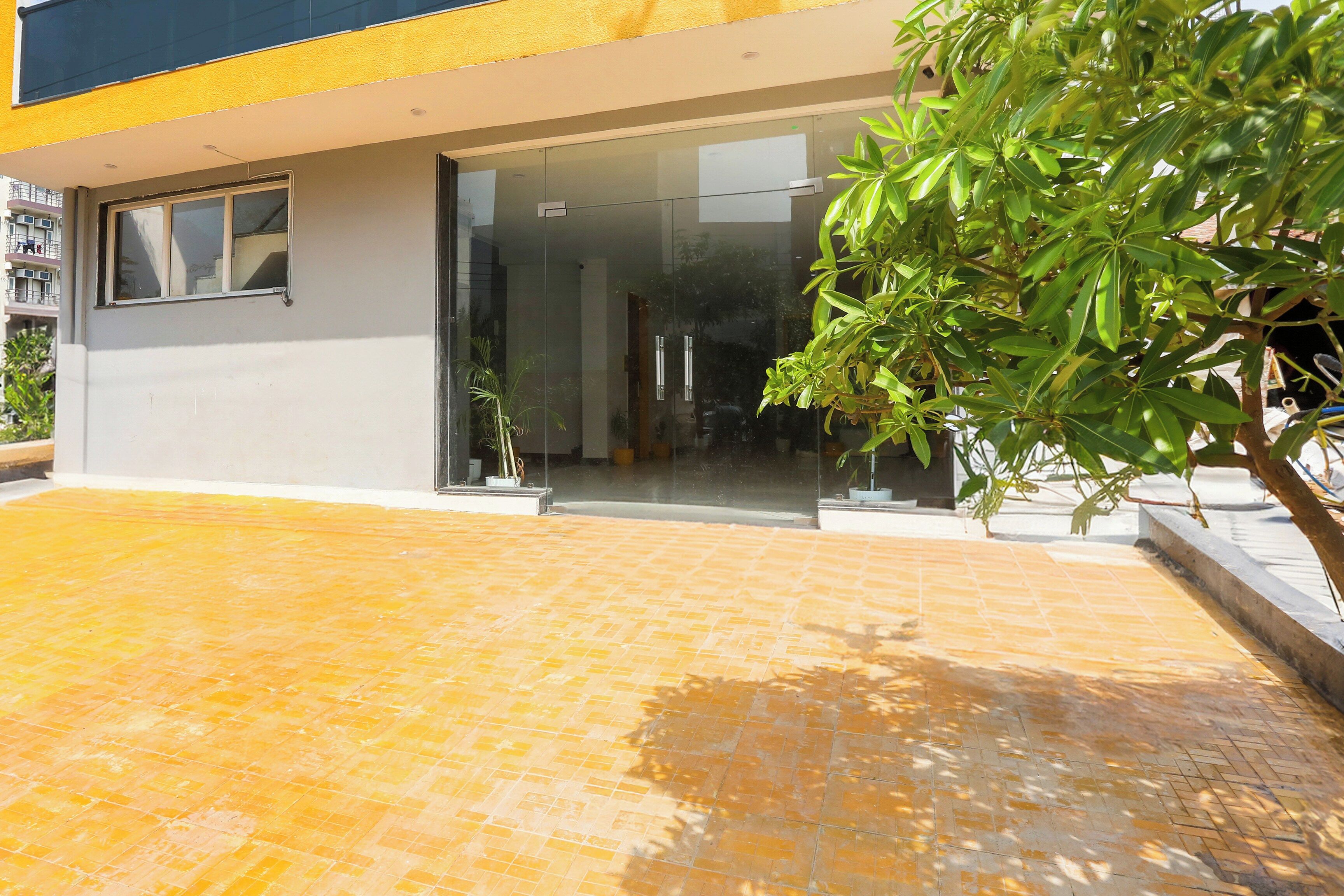 Un edificio moderno con entrada de vidrio, un patio con baldosas y una planta en maceta.