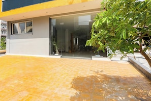 Un edificio moderno con entrada de vidrio, un patio con baldosas y una planta en maceta.