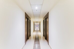 A long, narrow hallway with doors on both sides, leading to a brightly lit area at the end. - Collection O Civil Lines Near Old Bus (Bareilly)
