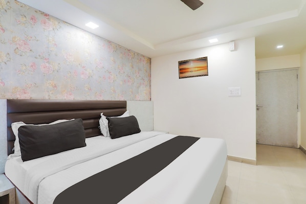 A hotel room with a large bed, a headboard, a floral wallpaper, a painting, and a door. - Collection O Civil Lines Near Old Bus (Bareilly)