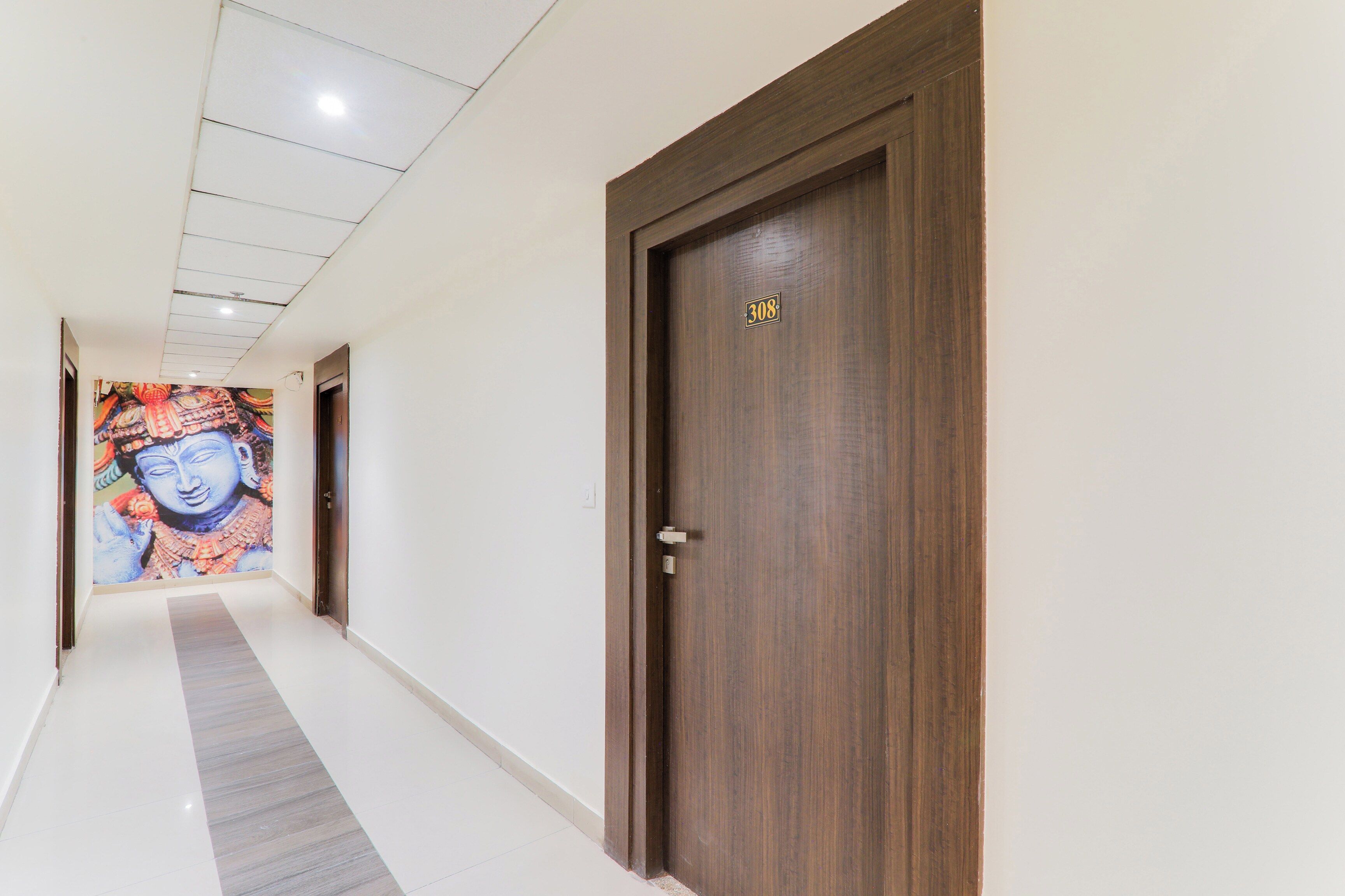 Un pasillo con una puerta de madera marcada con el número 308, piso de baldosas y un mural de colores en la pared.