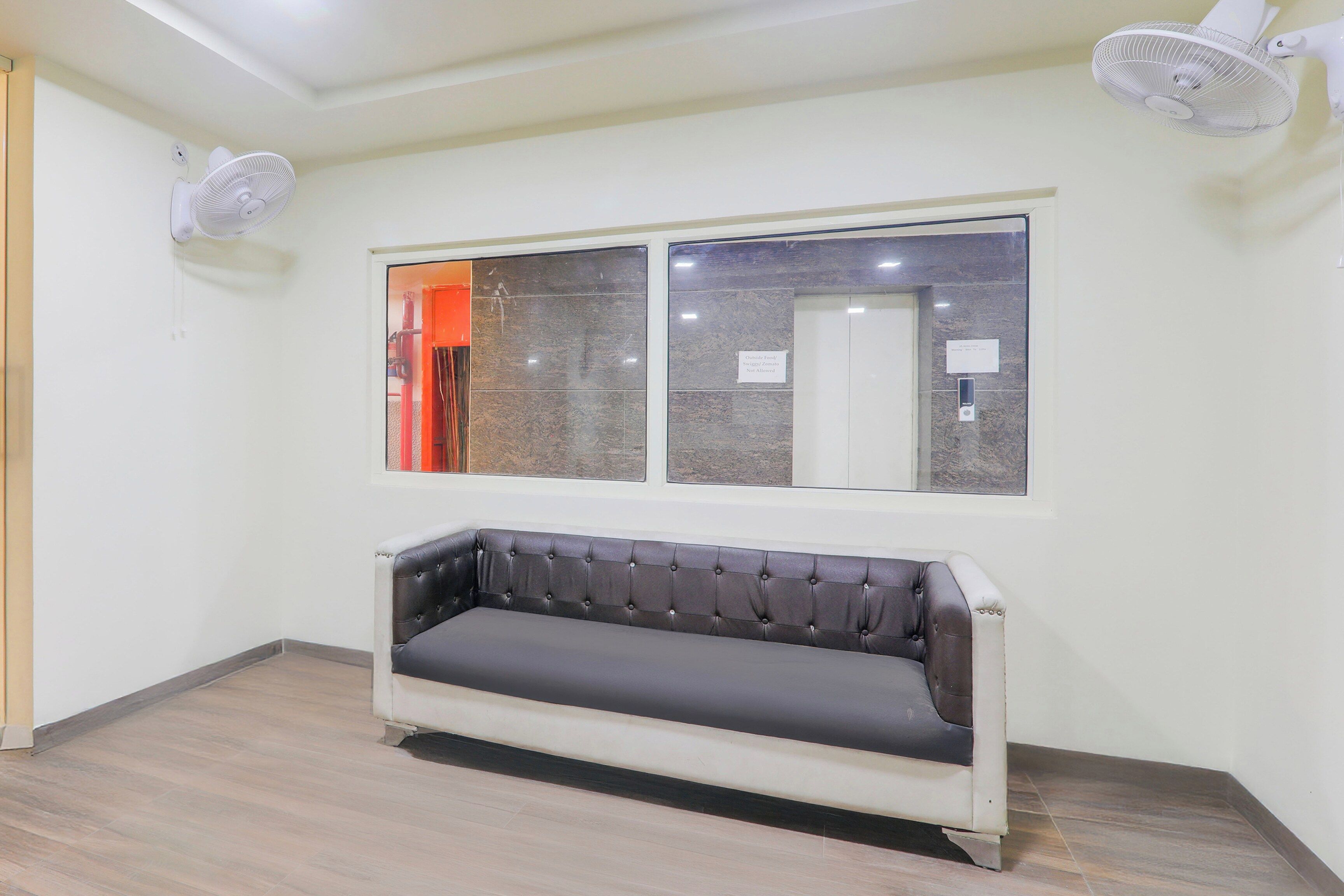 Una habitación con sofá, ventana y dos ventiladores fijos a la pared.