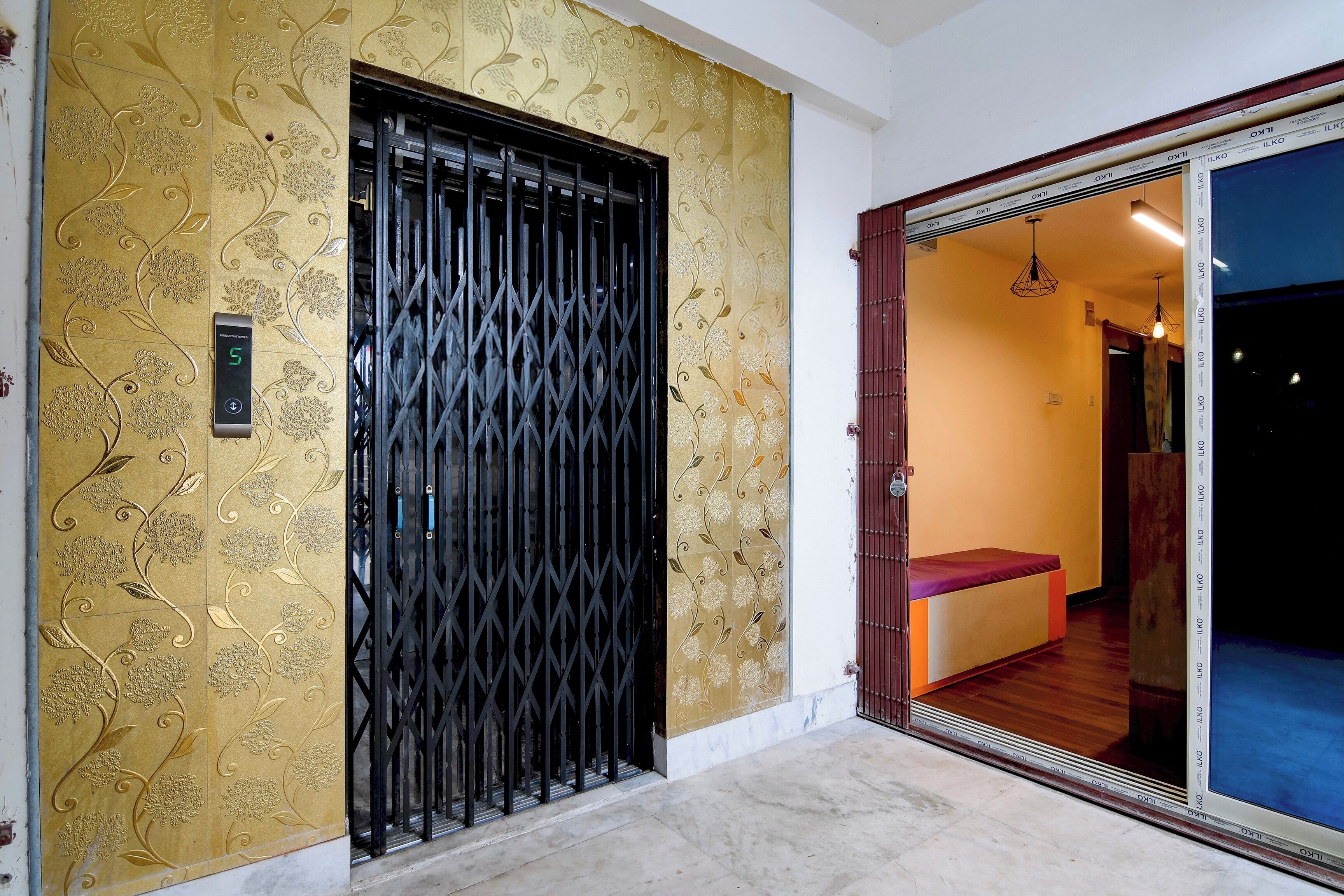 A room with a sliding glass door leading to a balcony, a bed with a red headboard, and a wall with a decorative pattern.