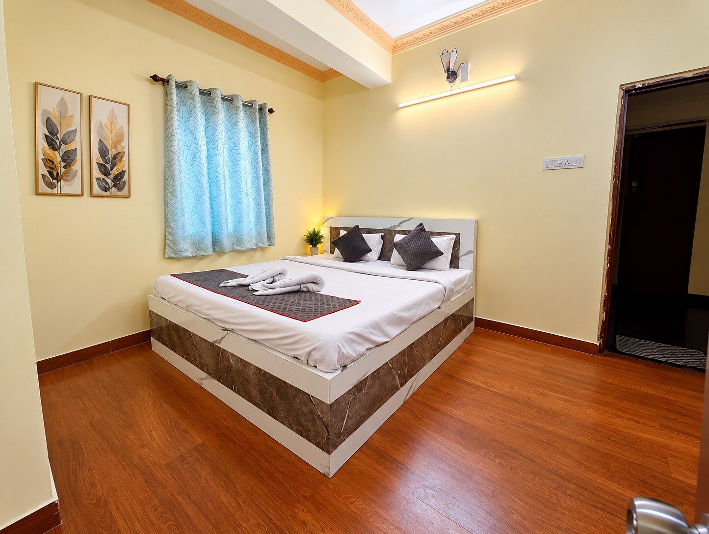 A hotel room with a bed, a nightstand, a wall-mounted lamp, and a window with curtains.