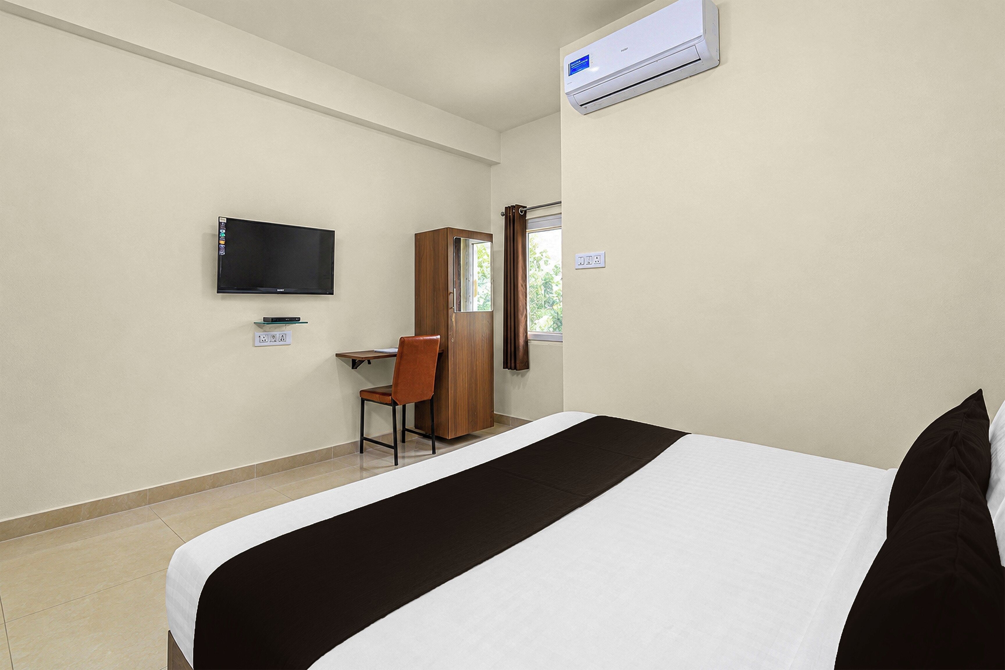 Habitación de hotel con cama, escritorio, silla, televisor y aire acondicionado.