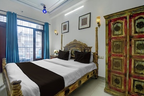 Ein Hotelzimmer mit einem großen Bett, einem dekorativen Kopfteil, einem Fenster mit blauen Vorhängen und einer Wand mit gerahmten Bildern.