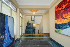 A hallway with a staircase, a large abstract painting on the right, and a ceiling light fixture. - Collection O Jal Mahal Jaipur (Jaipur)