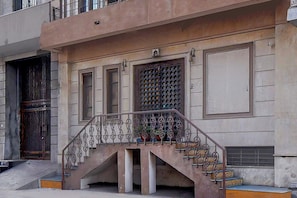 A building with a staircase leading to a landing, a large window with a decorative grille, and a door with a metal grille. - Collection O Jal Mahal Jaipur (Jaipur)