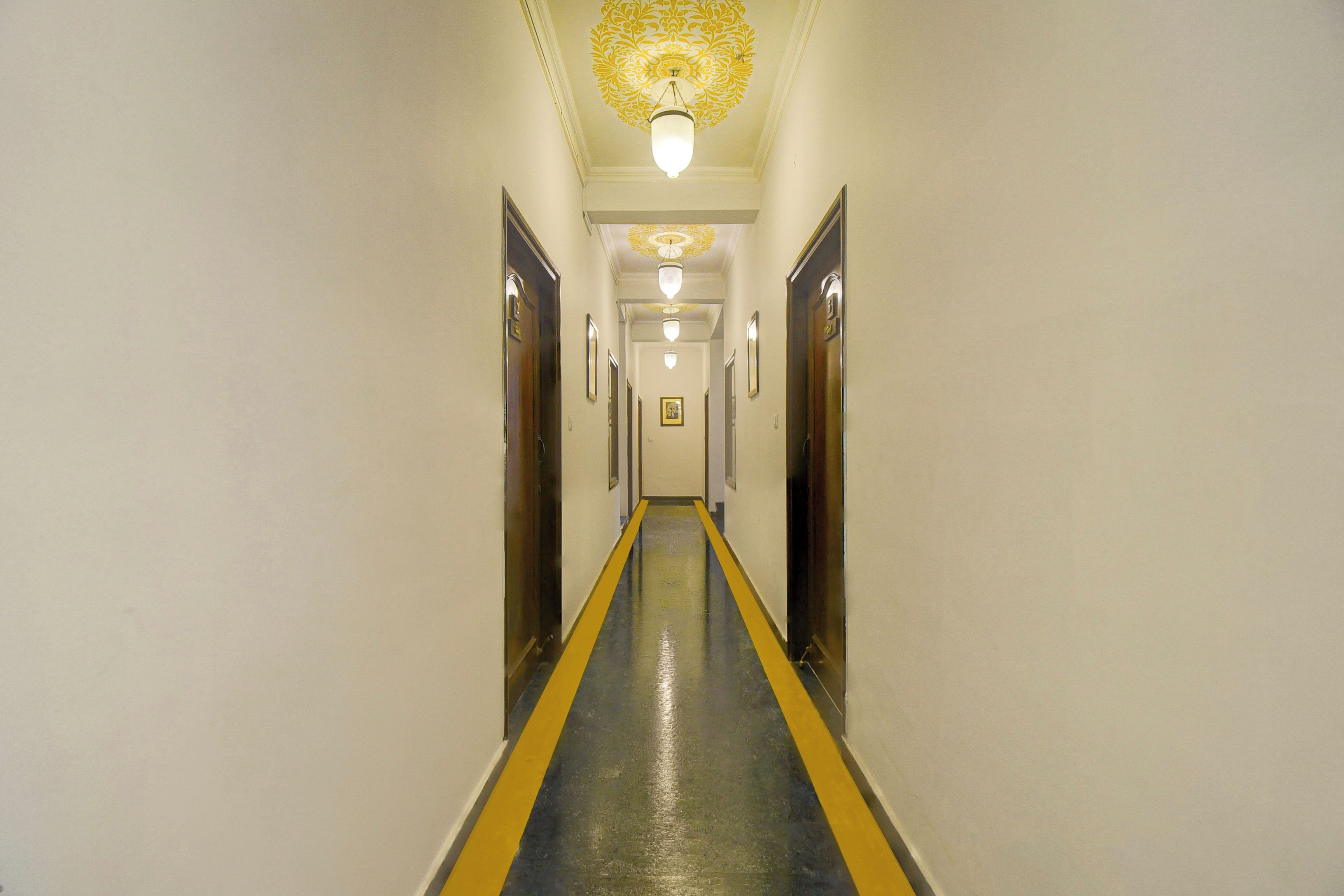 A hotel hallway with a central yellow line, doors on both sides, and a patterned ceiling light fixture.