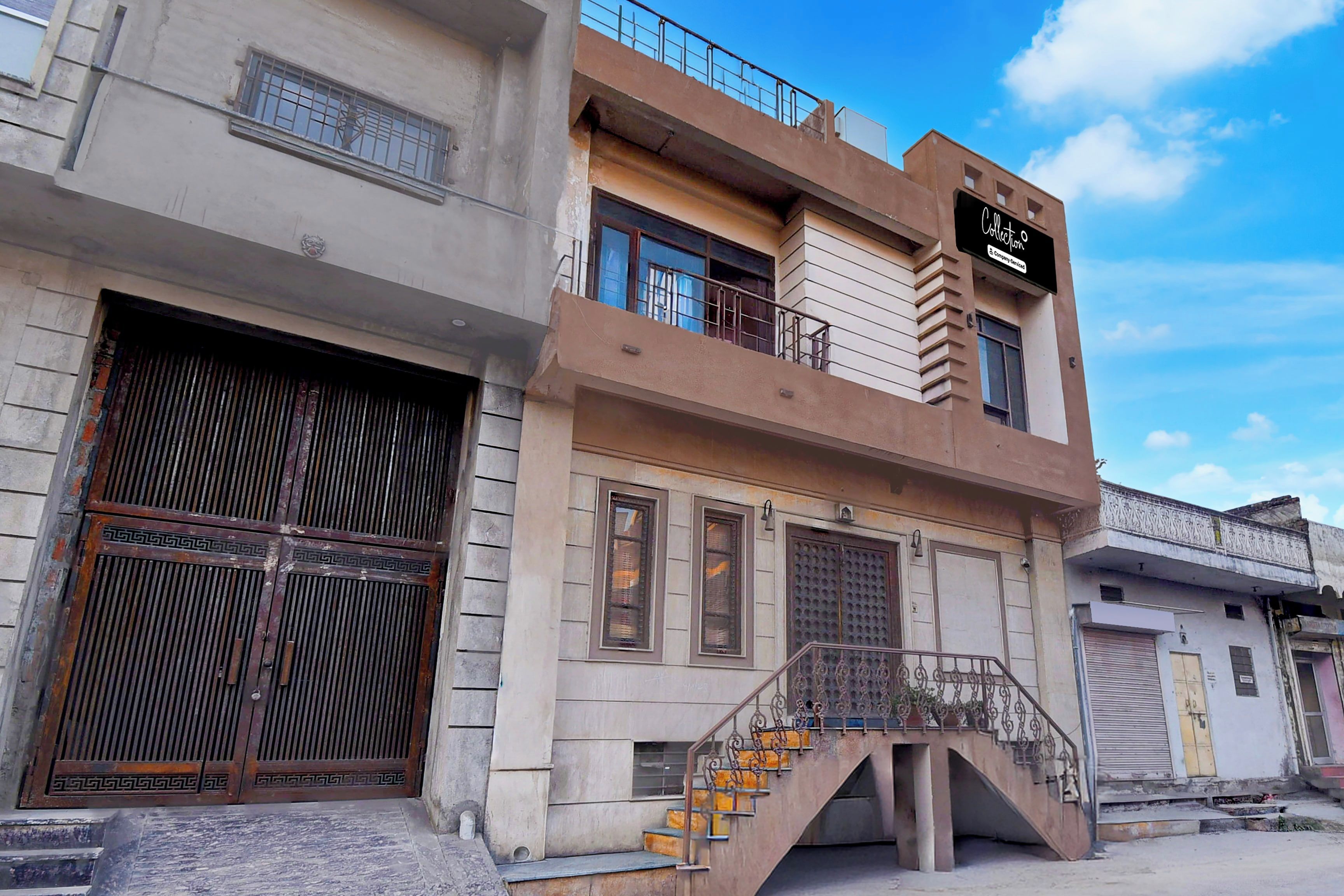 Un edificio de varios pisos con una escalera que conduce a la entrada, grandes portones metálicos y un letrero que indica un servicio de empresa.