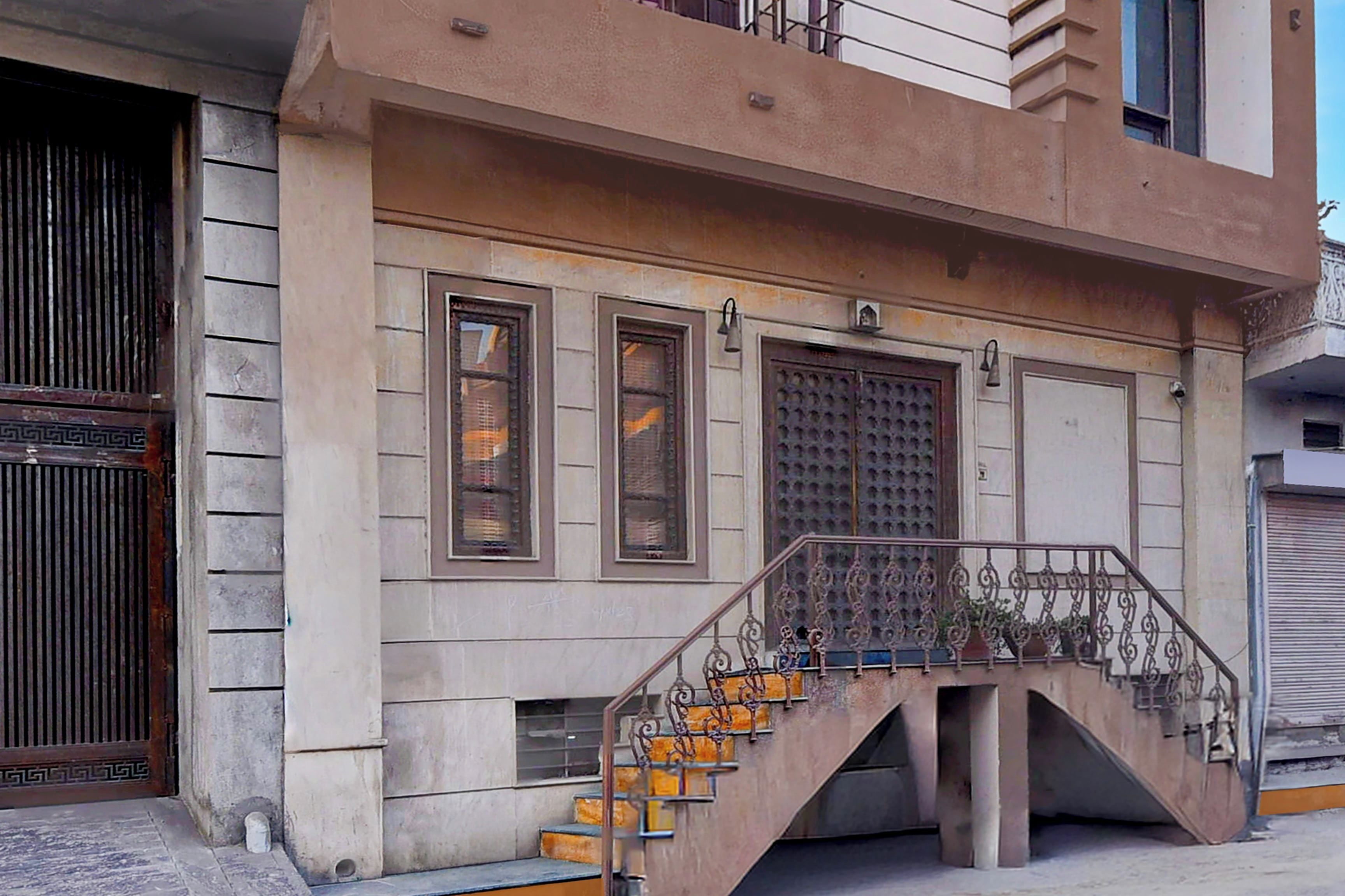Un edificio con una escalera que conduce a una plataforma, barandilla metálica y una puerta con diseño decorativo.