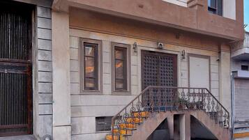 Un edificio con una escalera que conduce a una plataforma, barandilla metálica y una puerta con diseño decorativo.