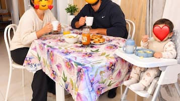 Un tavolo da pranzo con tovaglia floreale, una pianta in vaso e un bambino in seggiolone.