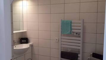 Et badeværelse med en hvid vask, en håndklædeholder med et blåt håndklæde og en sort opbevaringskasse med teksten 'BATH-H'.
