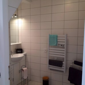 Et badeværelse med en hvid vask, en håndklædeholder med et blåt håndklæde og en sort opbevaringskasse med teksten 'BATH-H'.