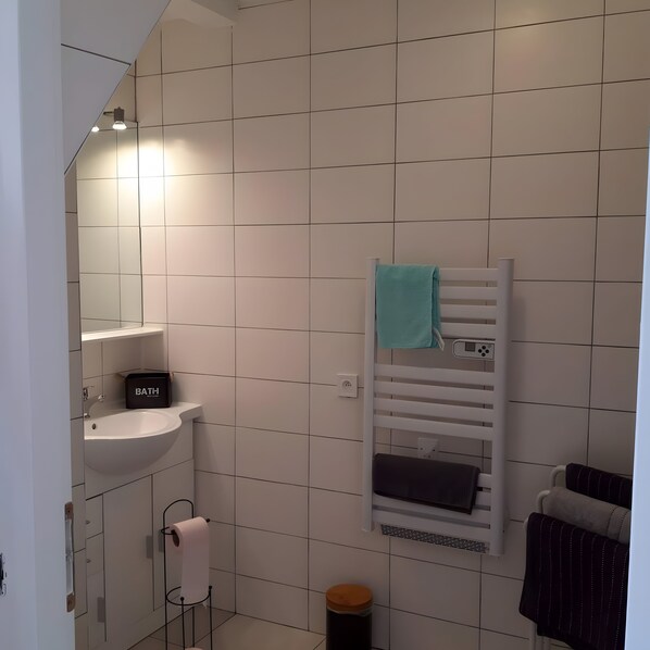 A bathroom with a white sink, a towel rack with a blue towel, and a black storage box labeled 'BATH-H'.