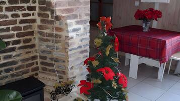 Een kamer met een open haard van baksteen, een kleine kerstboom en een eettafel met een rode tafelkleed.