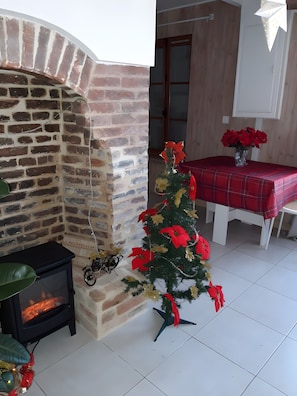 A room with a brick fireplace, a small Christmas tree, and a dining table with a red tablecloth. - Holiday Cottage 'Le Vélo Pêcheur' with Wi-Fi (Géraudot)