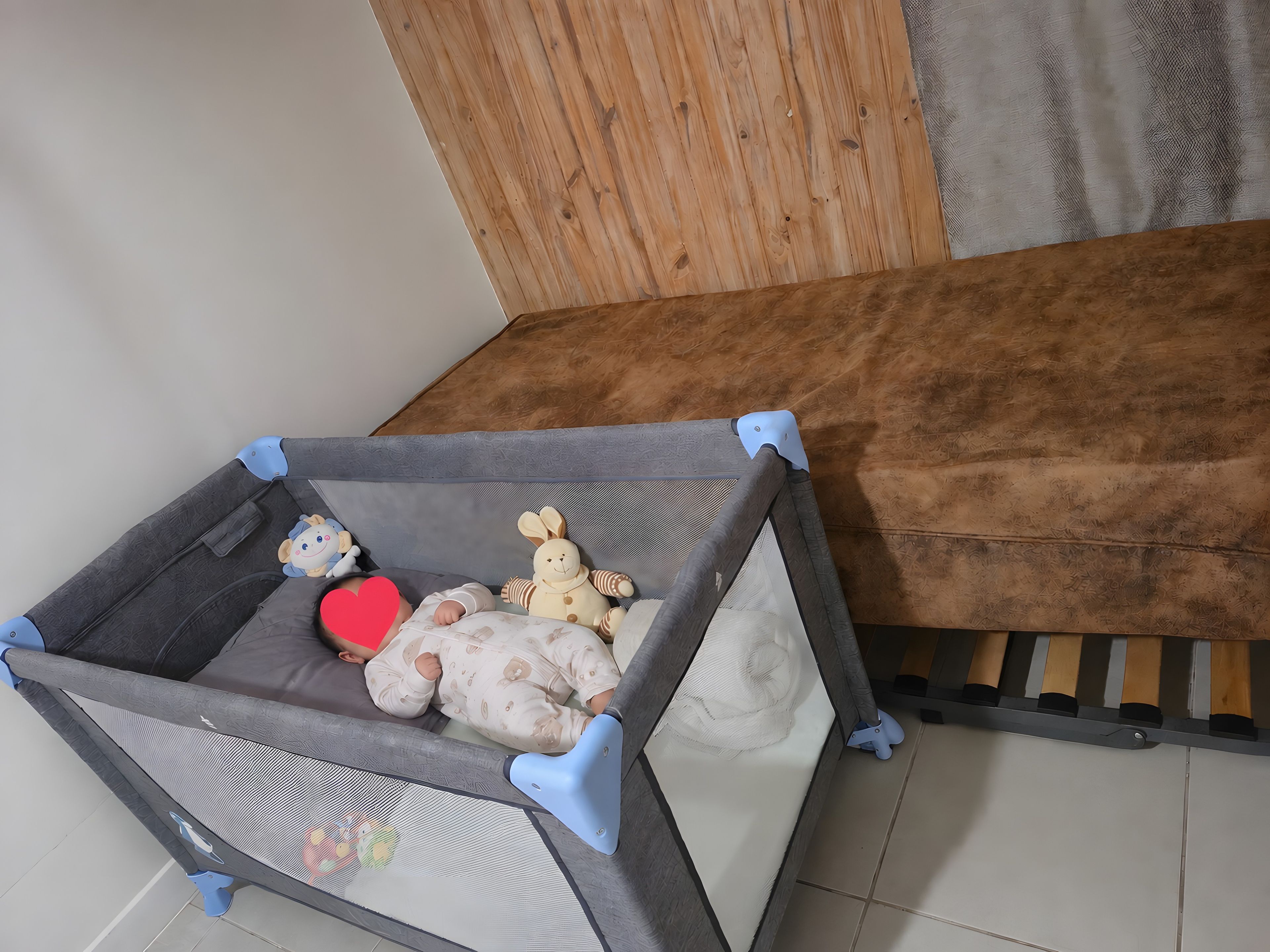 Un corralito para bebés con base de malla, un peluche y un cojín con forma de corazón rojo.