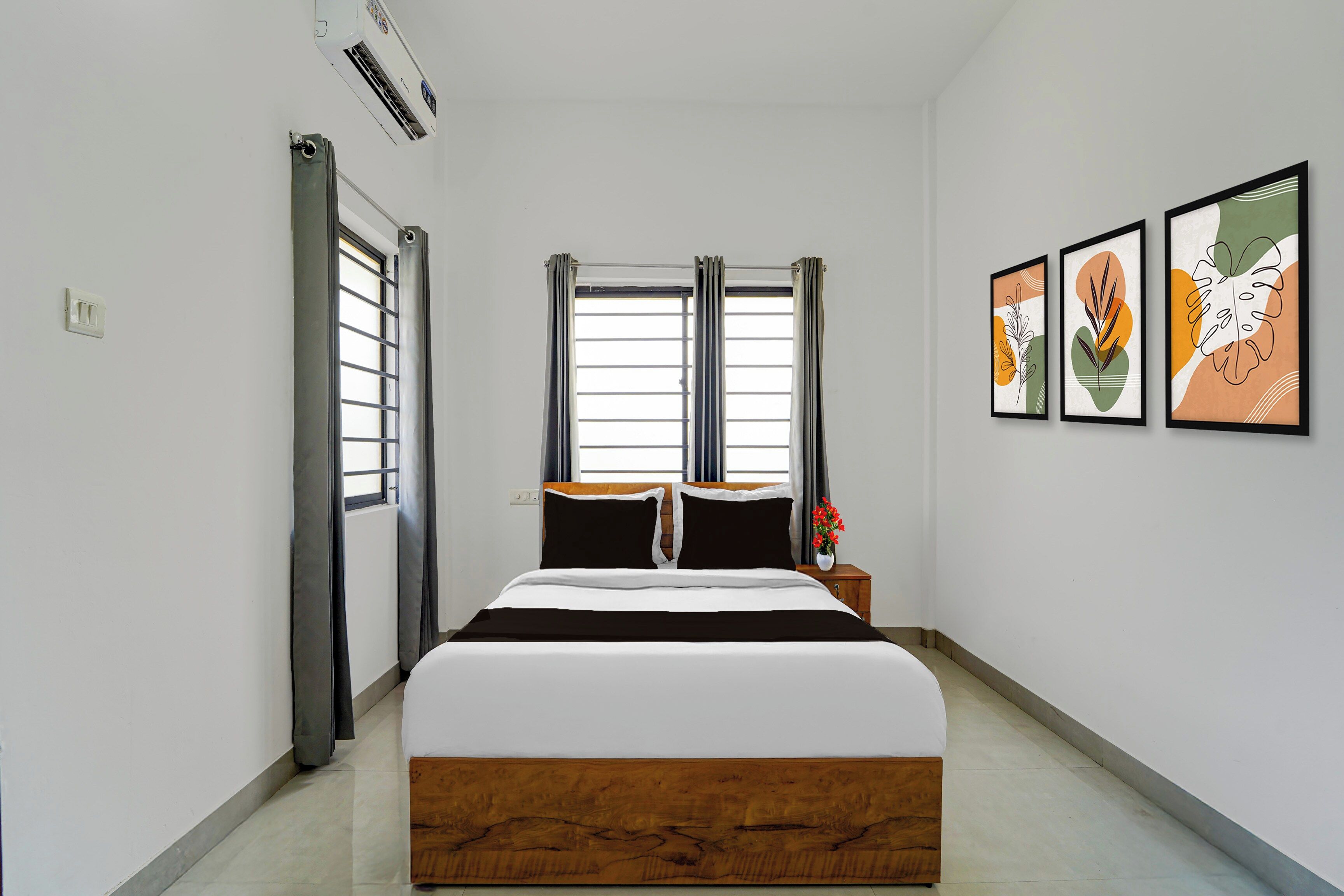 A hotel room with a bed, a nightstand, a window with curtains, and wall art.
