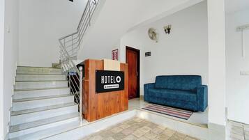 Zona de recepción de un hotel con un mostrador de madera, un sofá azul, una escalera y un letrero de salida de incendios.