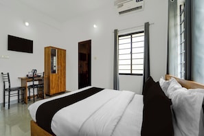 Habitación de hotel con cama, escritorio, armario, ventana y televisión de pantalla plana montada en la pared.