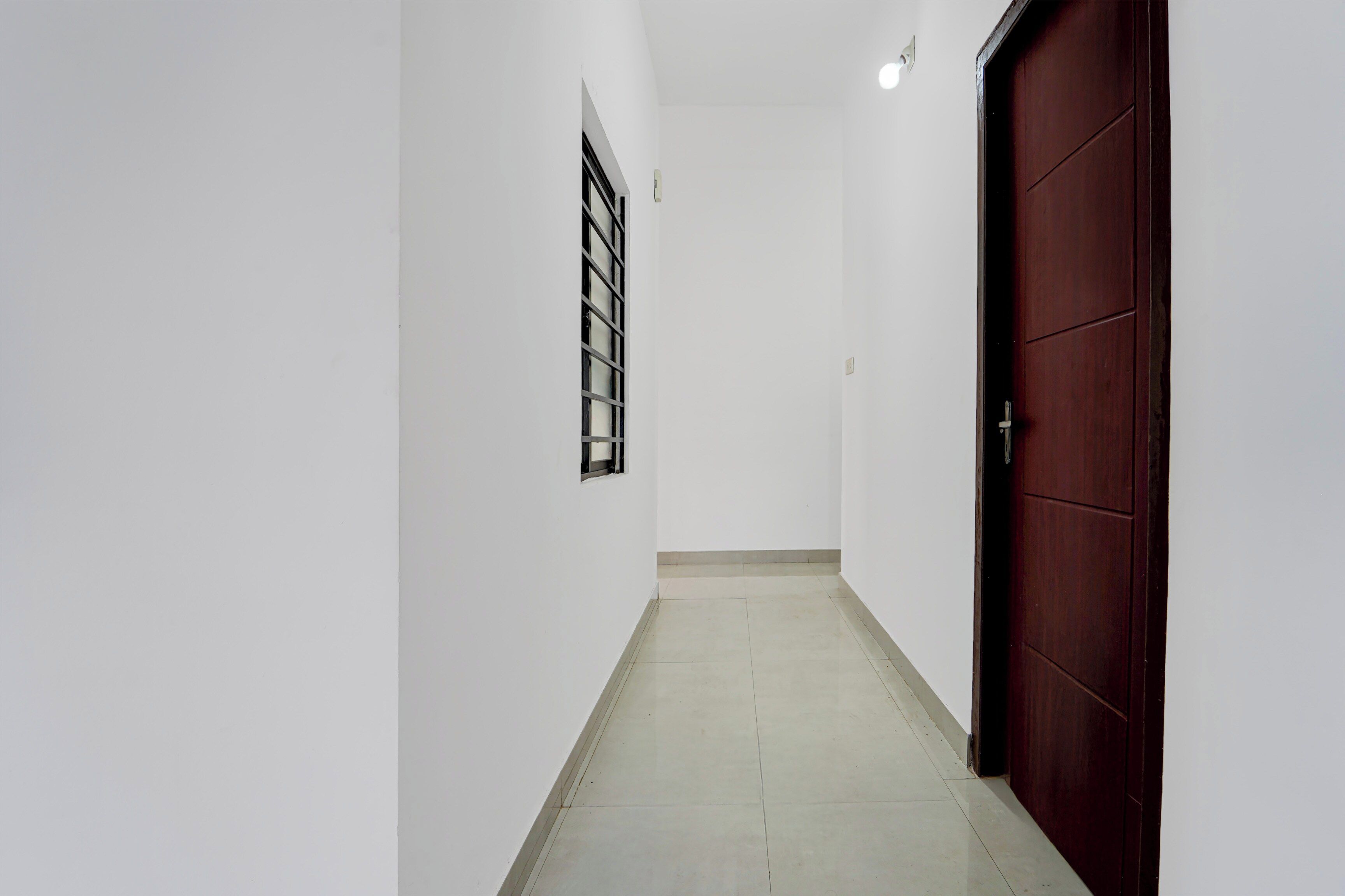 A corridor with a tiled floor, a door on the right, and a window on the left.