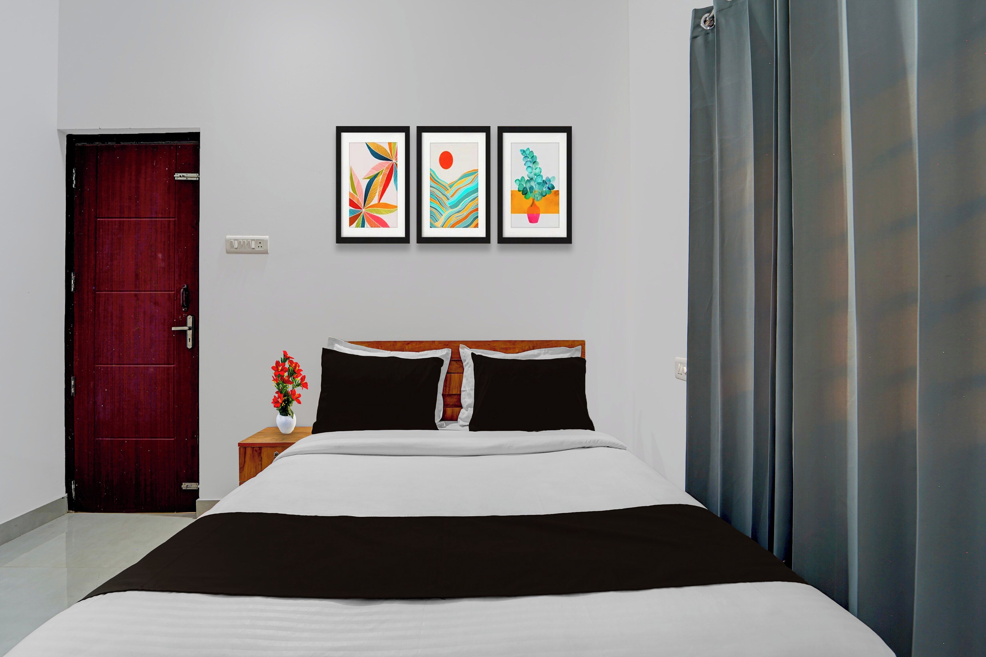 Ein Hotelzimmer mit einem Bett, einem Nachttisch mit Blumenvase und drei gerahmten Kunstwerken an der Wand.