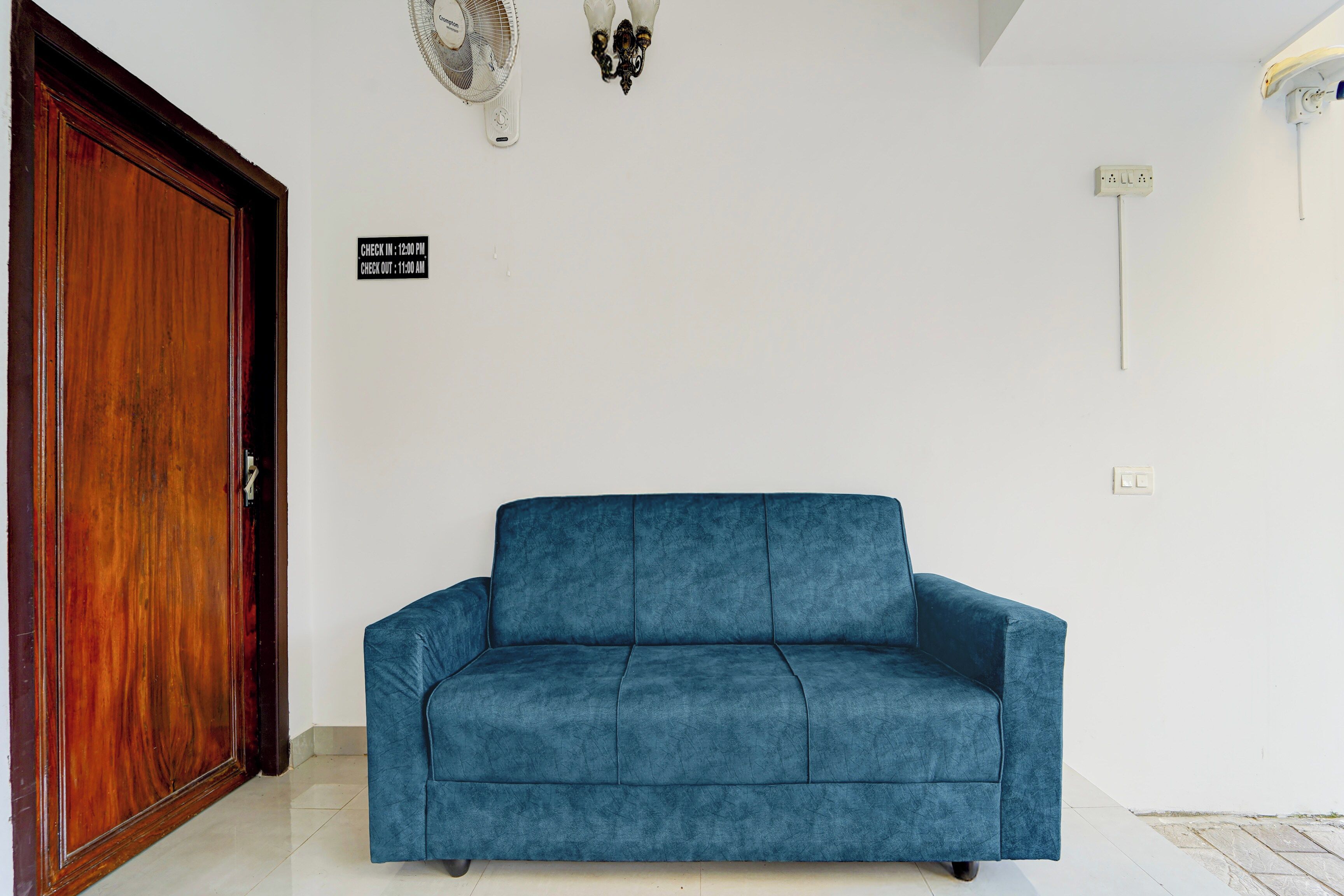 Una habitación con un sofá azul, una puerta de madera y un cartel en la pared que indica horarios de registro de entrada y salida.