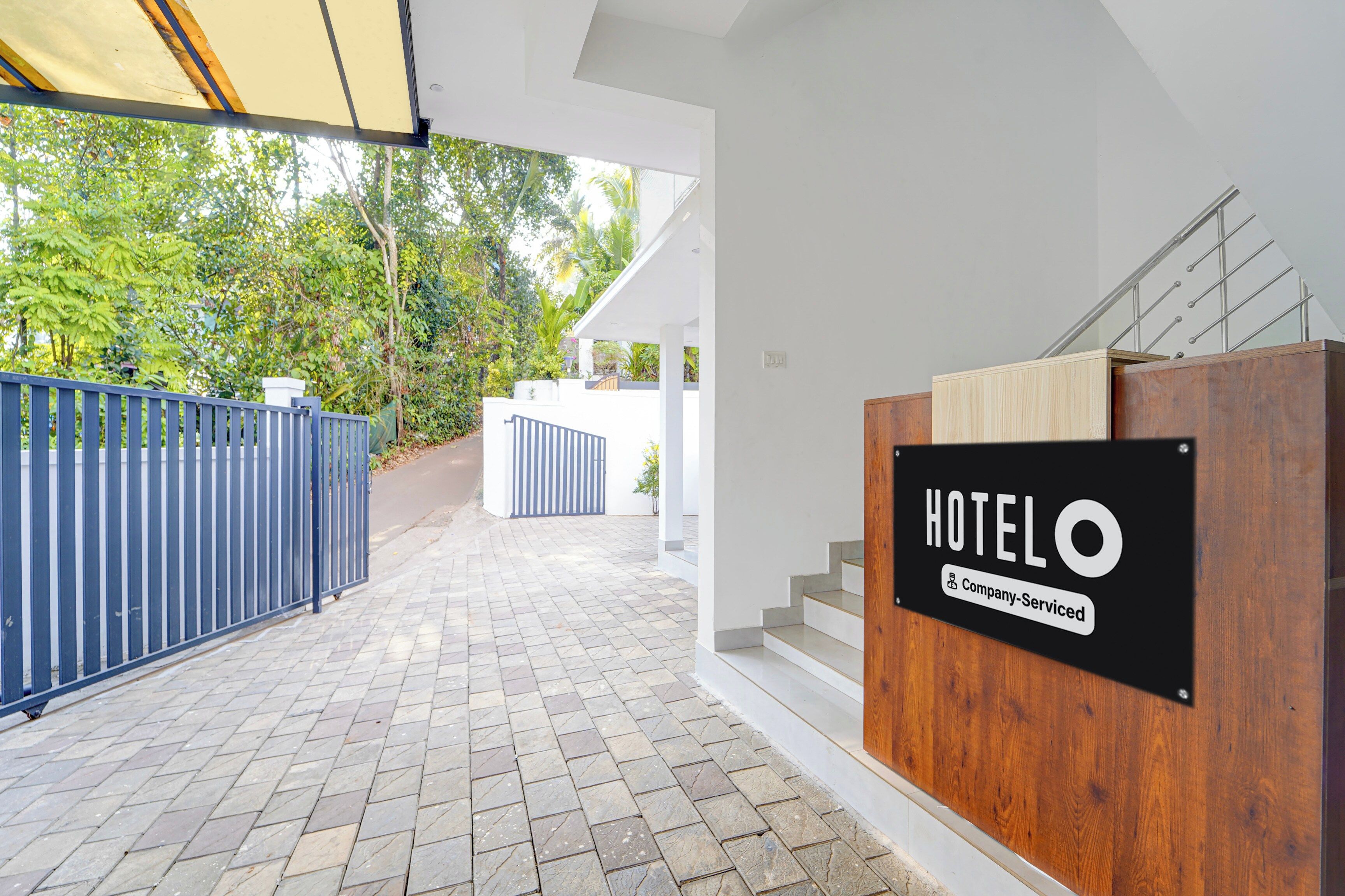 A hotel entrance with a wooden reception desk, a metal gate, and a staircase leading to the interior.