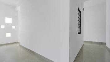 Un pasillo con paredes blancas y suelo de baldosas que conduce a una habitación con ventana y puerta.