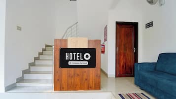 Un comptoir d’accueil d’hôtel avec un panneau indiquant qu’il est géré par l’entreprise, un escalier, une porte en bois et un canapé bleu dans l’espace salon.