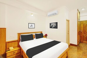 A hotel room with a bed, a bedside table with a telephone, a wall-mounted air conditioner, and a door. - Townhouse Mysore City Centre (Mysore)